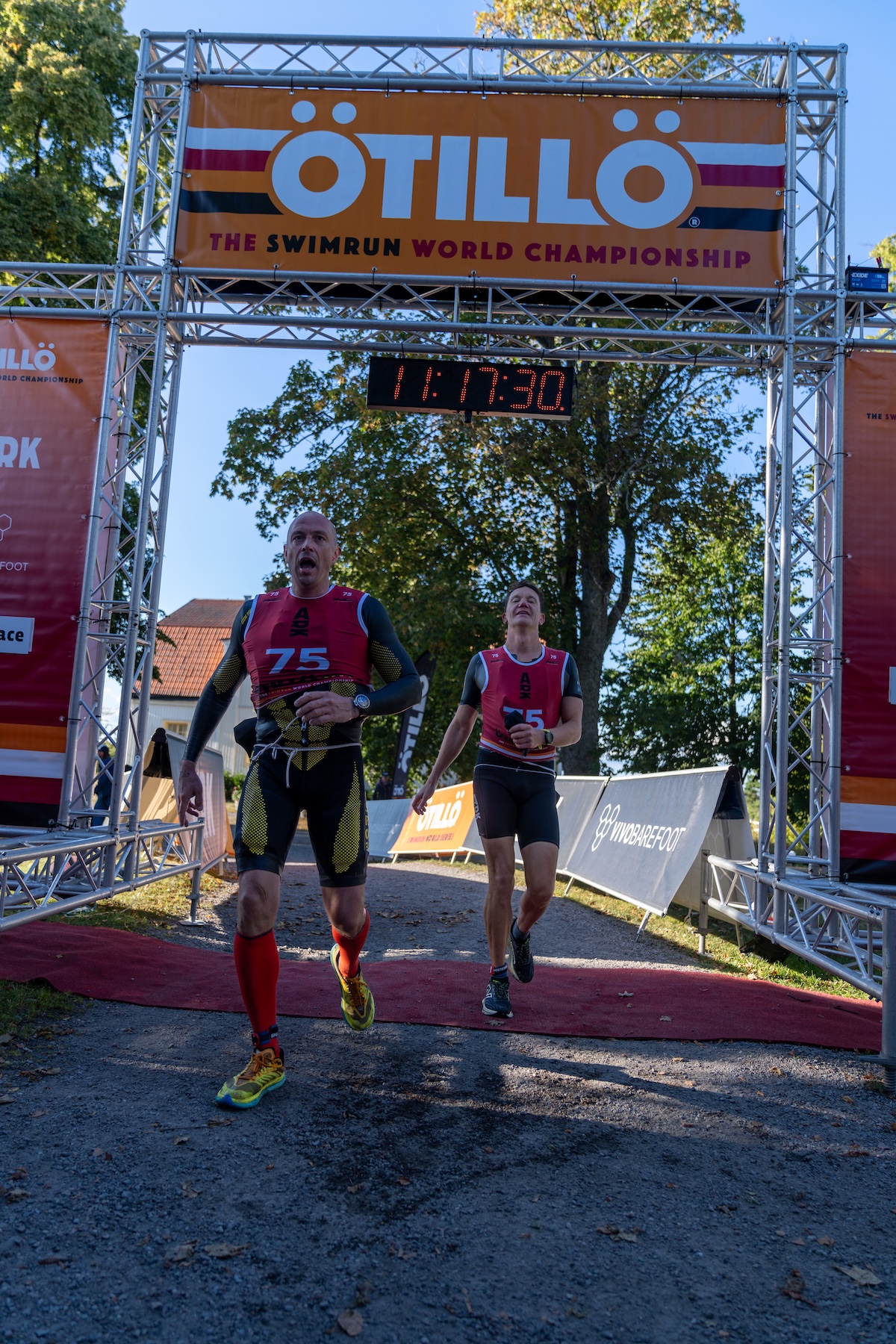 Två simmare i röda swimrun-dräkter korsar mållinjen vid ÖTILLÖ Swimrun World Championship